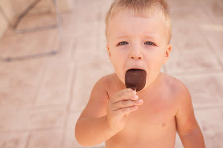 Small  sunburnt boy eating ice-cream outdoor in hor summer dayの写真素材