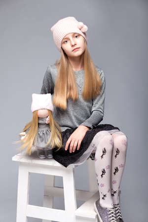 A small beautiful girl siiting on a chair with a doll in photostudioの写真素材