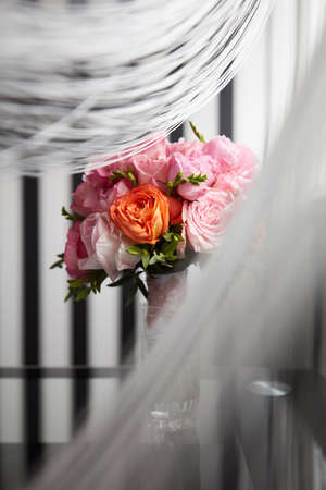 A Bucket of peony flowers standing on the glass table under the curtains near the windowの写真素材