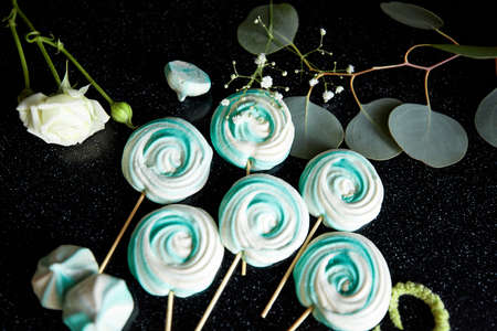Green and white sweets on the stick on the dark background decorated with some flowersの写真素材