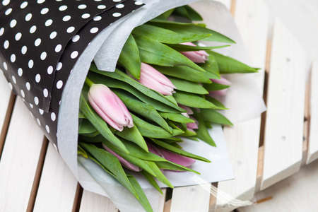 Beautiful spring pink tulips wrapped in stulish paper on a wooden backgroundの写真素材