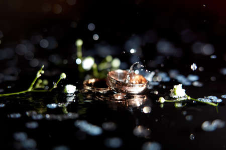 Golden wedding rings for bride and groom amond splashes of waterの写真素材