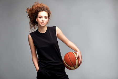 Very beautiful sportive girl model with afro curls and basket ball in sudio on neutral grey backgroundの写真素材