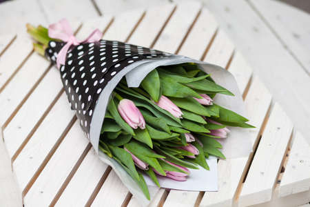 Beautiful spring pink tulips wrapped in stulish paper on a wooden backgroundの写真素材