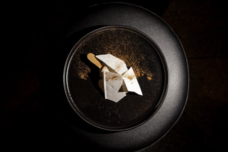 vanilla ice cream with powdered sprinkles on a black plateの写真素材