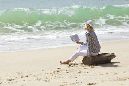 Woman with book is sitting on a stump by the wave line の写真素材