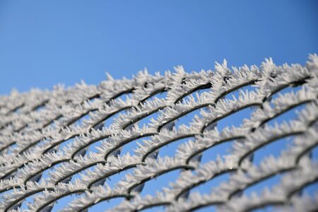 Plastic-coated wire fence covered with frost and hoarfrost, blue sky background. Frost.の写真素材