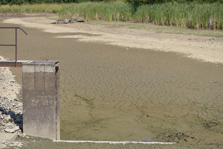 Empty and drained pond. Drought and no water in the landscape. Floodgate by the lake