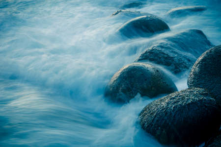 Close-up from waves swelling over rocks on the shore. Long exposure.の写真素材