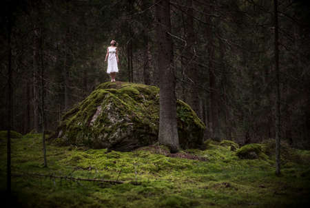 Girl alone in the forest standing on a big rock.の写真素材