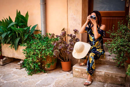 young woman with red hair sitting on a door step with a camera in from of her face and taking a...