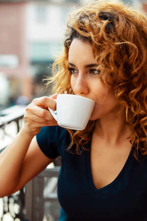 young moroccan woman, with curly brown hair, sitting in an outdoor cafe in Mainz, drinking coffee. High quality photoの写真素材