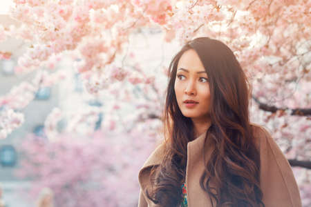 Young Asian woman, in front of blossoming cherry tree in the spring time . High quality photo