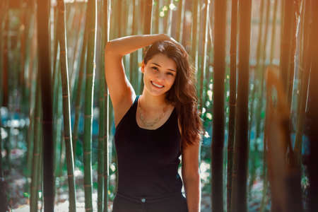Young Latina woman smiling at the camera, in front of bamboo and sunlight coming form the background. High quality photoの写真素材