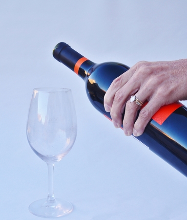 A woman s hand holding a bottle of red wine preparing to pour into a wine glass の写真素材