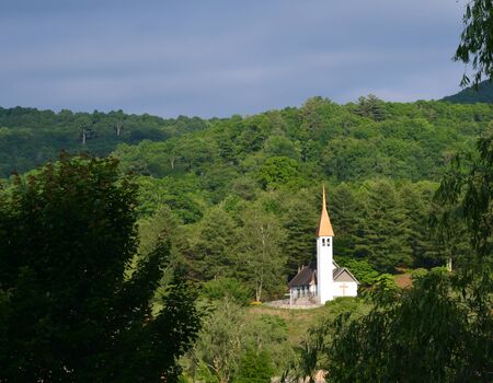 A small white country church in the middle of a lush green forest at sunset の写真素材