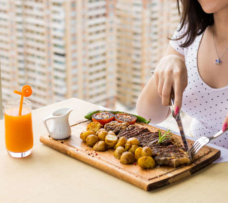 Woman eating tasty steak potato, vegetable on the wood plateの写真素材