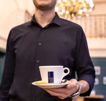 Waiter holding cup of coffee, tea at the restaurantの写真素材