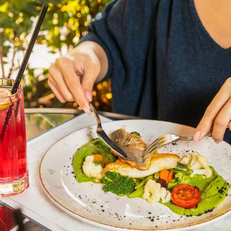 Woman eating fish meal with red cocktailの写真素材