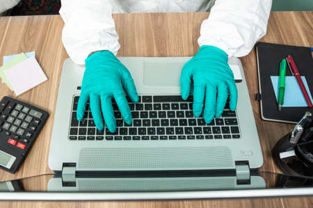 Disinfection man with special white suite working on laptop at office top view
