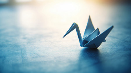 Single origami crane is standing on a blue surface with a bright backlightの素材