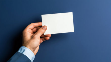 Hand holding a blank white card on a blue background, ideal for adding text or graphicsの素材