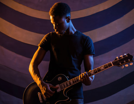 A young man stands on stage, deeply focused as he plays an electric guitar. Colorful lights create a vibrant atmosphere in the background during a live performance, captivating the audience.の素材