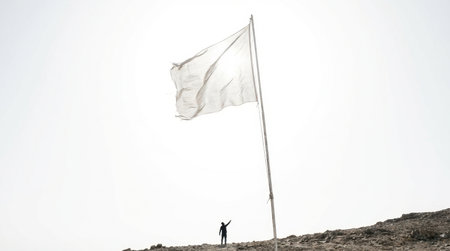 A large white flag waves gently atop a hill during sunset. A person stands below, stretching their arms upward, symbolizing hope and unity in a serene landscape.の素材