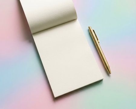 A blank notepad lies open next to a gold pen against a soft pastel background. This setting invites writing ideas, taking notes, or planning tasks. The peaceful colors enhance focus and creativity.の素材