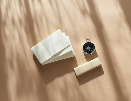 Blank notes and a small compass are arranged on a light beige surface. Shadows from nearby objects are playing softly across the scene as daylight shines.の素材