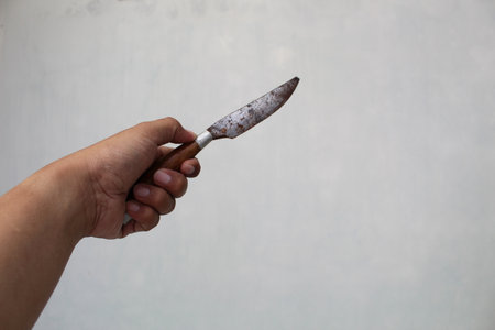 left hand holding a knife against a white wall background. crime illustrationの写真素材