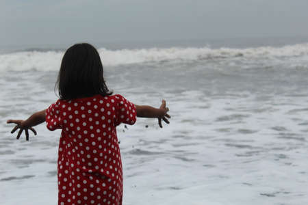 The girl in a red dress stands on the seashore and looks at the sea.