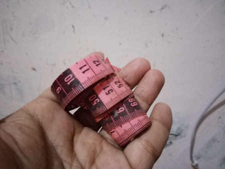 Sewing, sewing, tailoring and handmade concept - close up of hand holding pink measuring tape