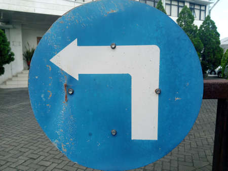 A blue sign with a white arrow pointing to the left on the streetの写真素材