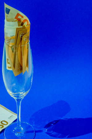 Sparkling wine glass filled with banknotes, blue background.の写真素材