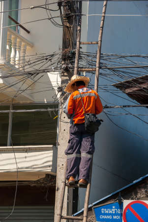 14.11.2011, Chiang Mai, Thailand. A cable technician stands on a ladder and works on a power pole.のeditorial素材