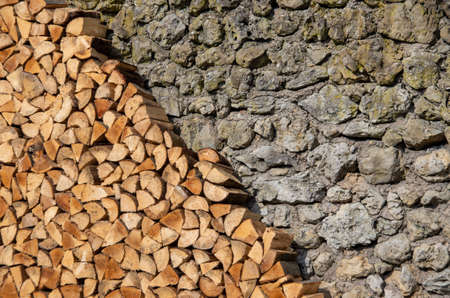 Firewood stacked in front of limestone wall as texture or background