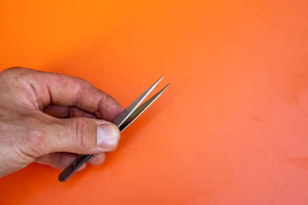 Male hand with tweezers in front of orange background. Copy Space on the right side.の写真素材