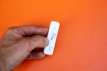 Hand with a positive test result of a rapid test for self-application in front of an orange...