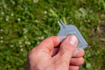 Male hand with tick card for removing ticks in front of green meadow. Concept Picture for tick bite.