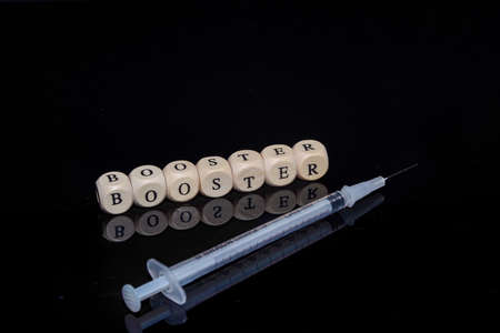 Bamberg, Germany - 16.11.2021. Cubes with inscription Booster and vaccine syringe against a black, reflective backgroundのeditorial素材