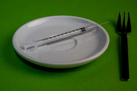 Vaccination syringe on a white plate in front of a green background, cake forkの写真素材