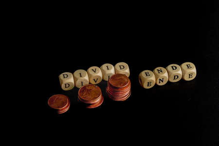 Staples of coins with wooden letters cubes forming the word "Divid Ende" in german language, concept picture for the end of dividend.の写真素材