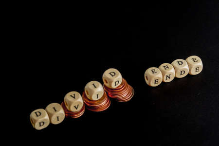 Staples of coins with wooden letters cubes forming the word "Divid Ende" in german language, concept picture for the end of dividend.の写真素材
