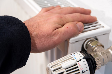 Hand lies on radiator, thermostat on level 3の写真素材