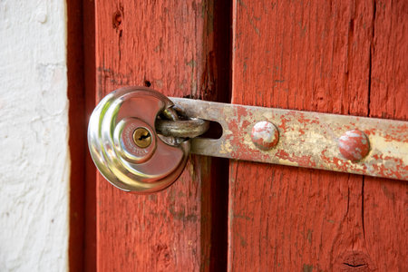 A sturdy padlock is securely attached to a vibrant red wooden doorの写真素材