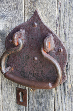 A weathered and rusty door handle that is attached to a wooden doorの写真素材