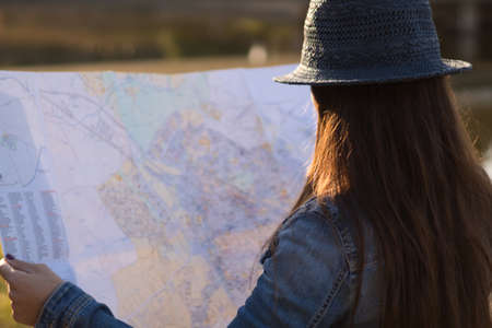 Young woman with blue hat and denim jacket consulting a map during a trip in the foreground.の写真素材