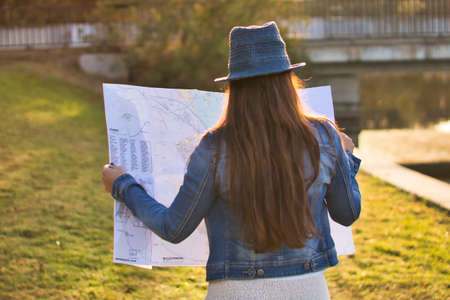 Young woman with blue hat and denim jacket consulting a map during a trip outside with an unfocused background.の写真素材