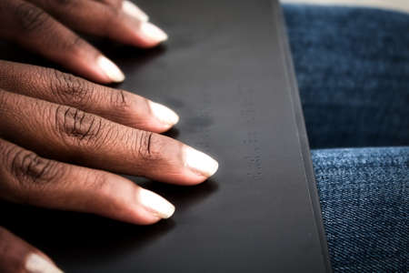 Detail of african american womanÂ´s hands reading braille in a black book in closeup.の写真素材